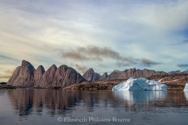 Rocky landscape with cloudy sky, still water, and floating icebergs