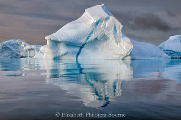 Pinnacle iceberg with blue vein floating in still water with reflection