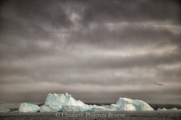 Long white iceberg against a stormy gray sky and ocean in Greenland