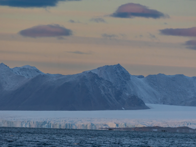 Photograph of a glacier edge with mountains and a peach and purple sky