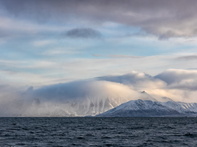 Photograph of a cloud covered mountains against a dramatic sea