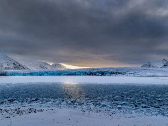 Photograph of a dark sky with a blue glacier and ice-filled lagoon in front