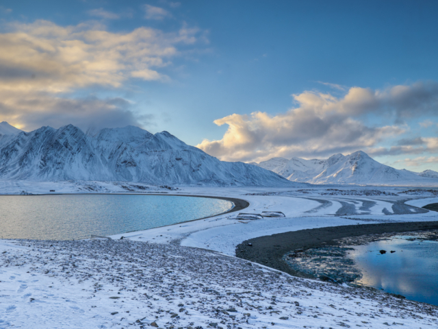 Photograph of an isthmus and two bays with cloud covered mountains in the distance
