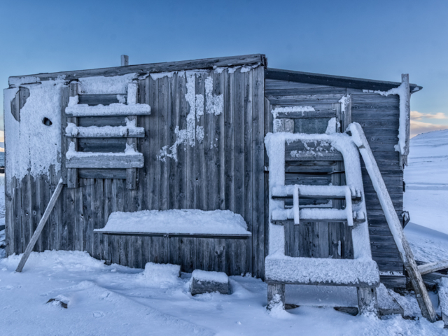 Photograph of a small wooden cabin in blue Arctic light