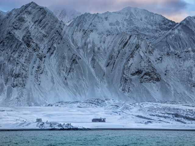Pohtograph of black and white mountains with strange geology and two small cabins by the shore