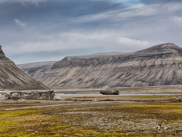 Photograph of a bleak landscape with an abandoned boat and twisted train tracks under a brooding sky