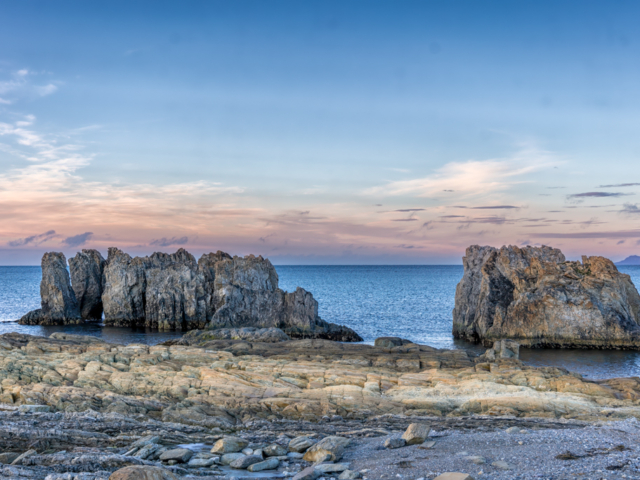 Photograph of strange rocks rising out of the sea with a pink and blue sky