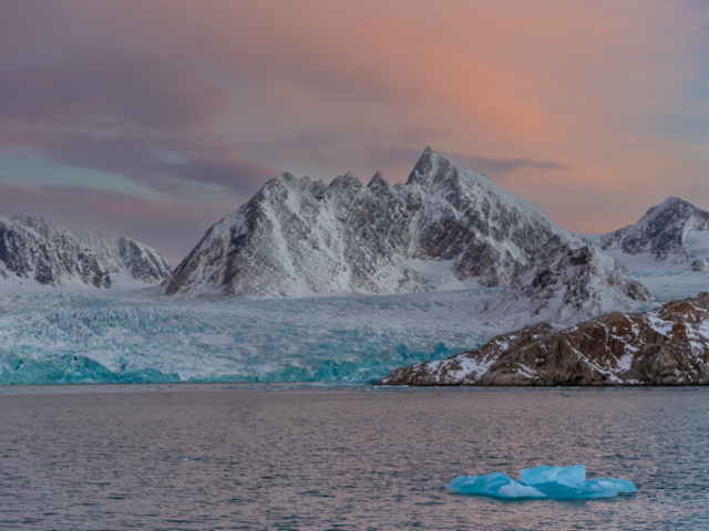 Photograph of mountains and blue glacier front against a sunset sky of pink and purple