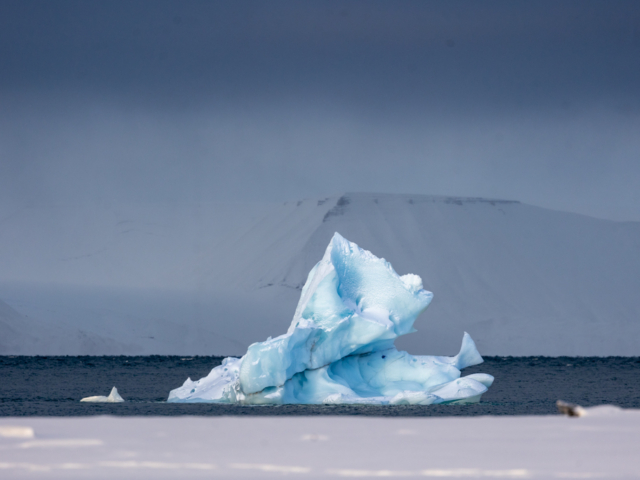 Photograph of a white and blue iceberg against a dark grey background.