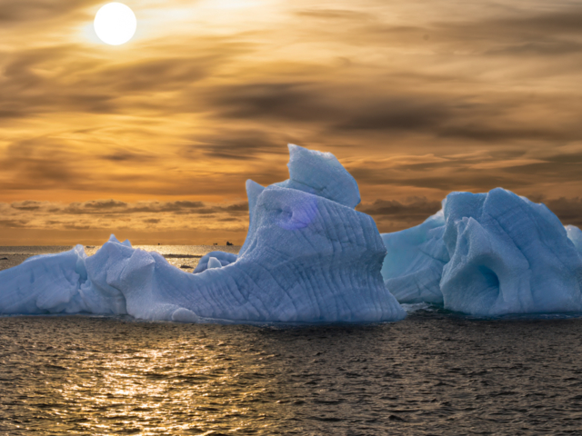 Photograph of blue iceberg against a yellow and gold sky