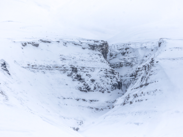 Photograph of a deep snowy canyon marked by black rocks.
