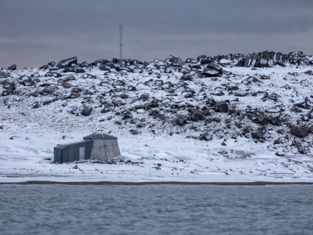 Photograph of a gray wooden cabin on a rocky show on a dark day