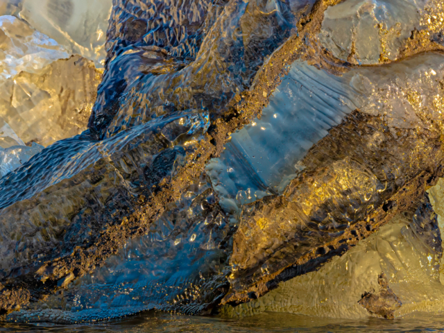 Photograph of a close up of iceberg ice that is blue and orange and sreaked with dirt.