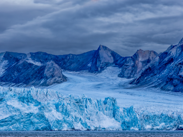 Photograph of an omnious sky over a very blue glacier front.