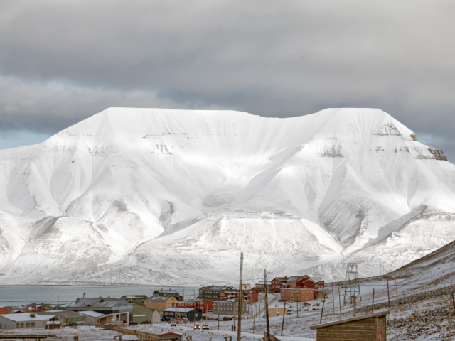 Hiorthfjellet and Longyearbyen Snow covered mountain in a cloudy sky forms the background for the small arctic town of Longyearbyen