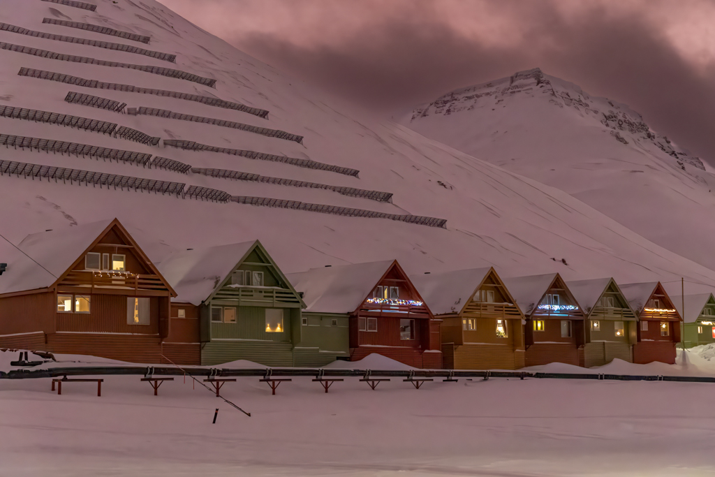 Spisshusene, or the Pointy Houses Photograph of colorful pointy houses against a backdrop of pink snowy mountains.