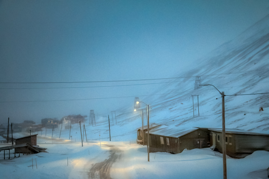 Road from Nybyen in a storm hotograph in blue light of a small houses and road in snow during a storm