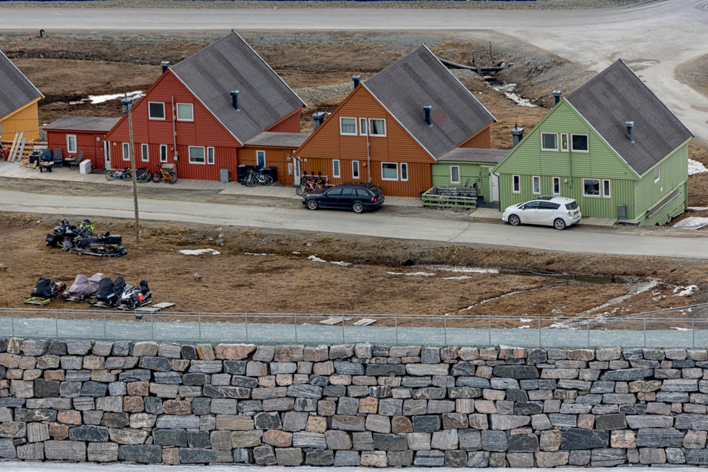 The Last Avalanche Fence Photograph of a large stone wall with three colorful pointed houses beyond it